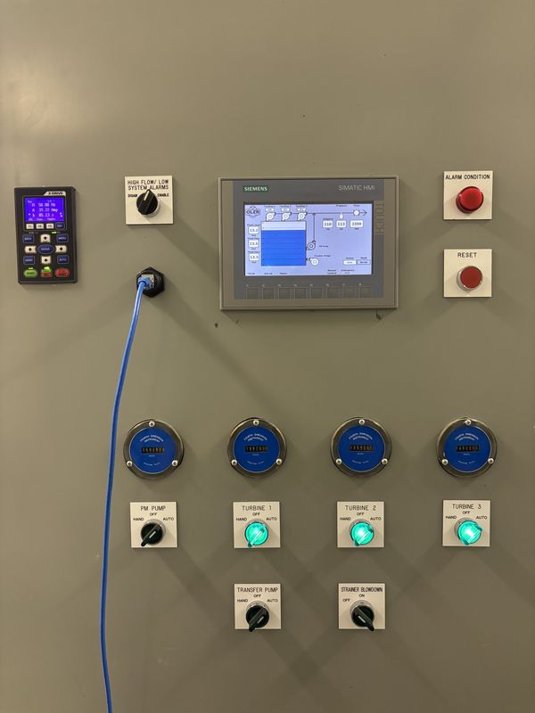Grey pump station cabinet door with a drive keypad, a Siemens touch screen, an alarm light, a reset button, four hour meters and pump switches lit green