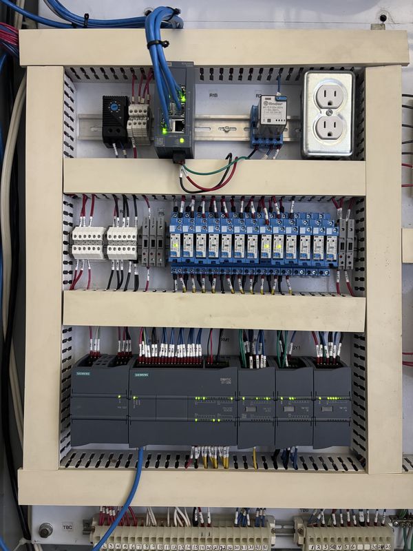 New Siemens S7-1200 PLC with expansion modules, a row of blue Finder relays, a network switch and labelled wires on the same backplate
