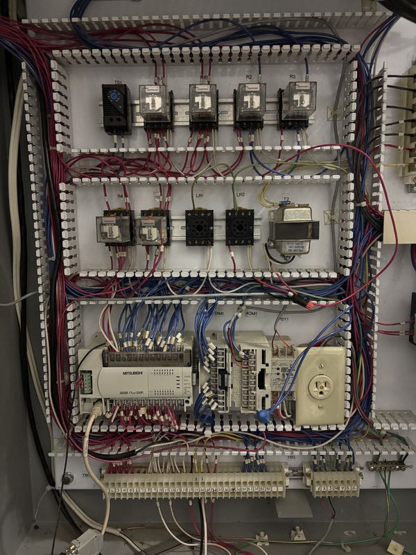 Old control backplate with a Mitsubishi FX2N-32MR PLC, rows of plug-in relays and red and blue wiring