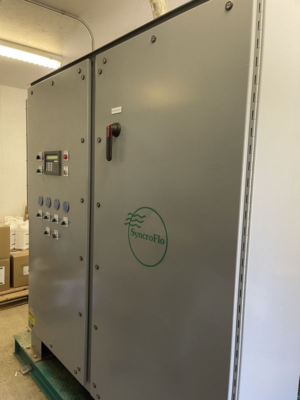 Grey SyncroFlo pump station cabinet with a small keypad and text display, four hour meters and a row of switches on the left door